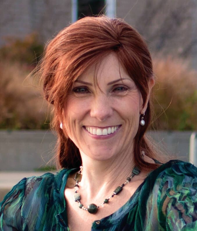 Ann Betz PCC headshot photo, smiling woman with red hair wearing cool toned top outside