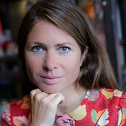 Anna-Marie Watson PCC headshot photo, woman with brown hair and blue eyes resting chin on her hand wearing colorful top