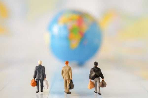 three human figures with bags walking toward a blurred globe