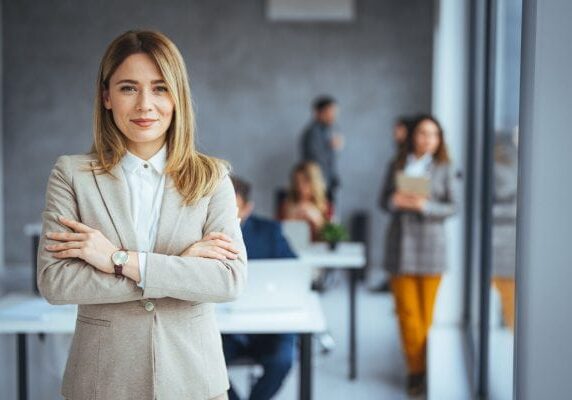 coach smiling in an office with people blurred and working behind her
