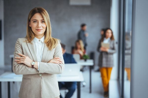 coach smiling in an office with people blurred and working behind her