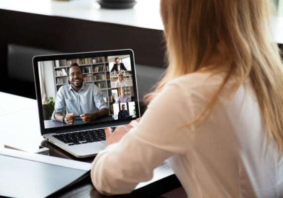 woman videoconferencing with five people on a laptop at a table