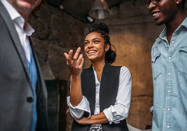 A professional woman smiling brightly, engaged in an animated collaborative coaching session with two male colleagues who are out of focus.