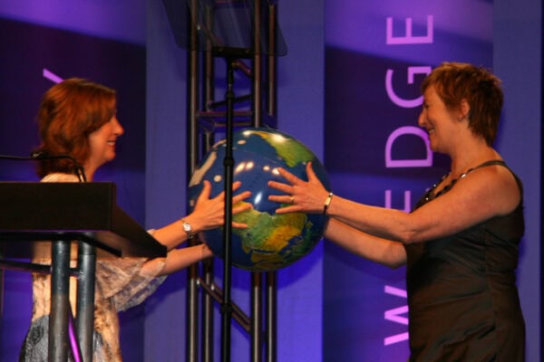 A woman passing a globe to another woman, symbolizing the transition of leadership to the 2009 ICF Global Board President.