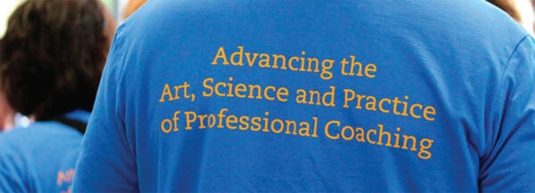 The back of a blue T-shirt worn by a person, displaying the phrase "Advancing the Art, Science, and Practice of Professional Coaching" in yellow text.