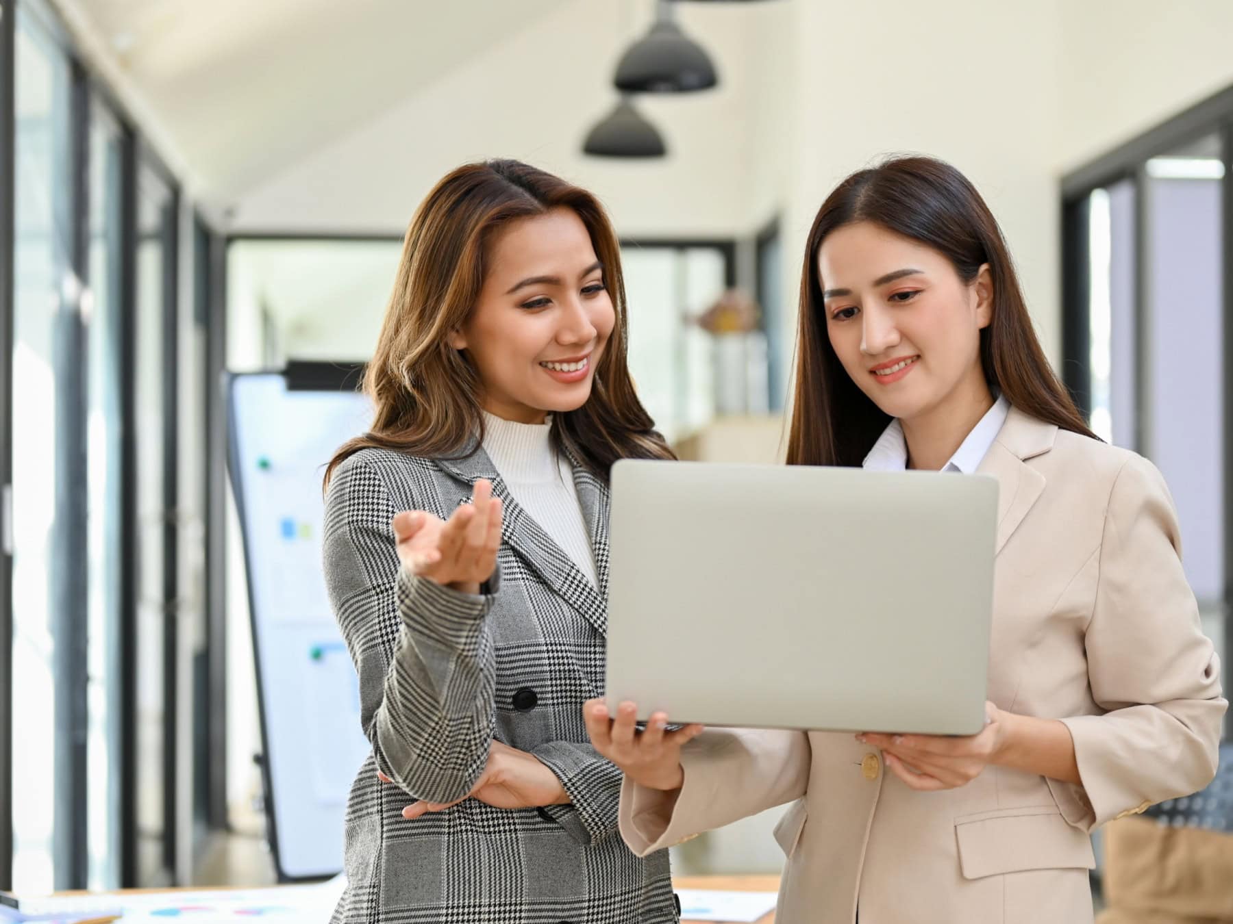 Two woman look at the computer while in an office setting.