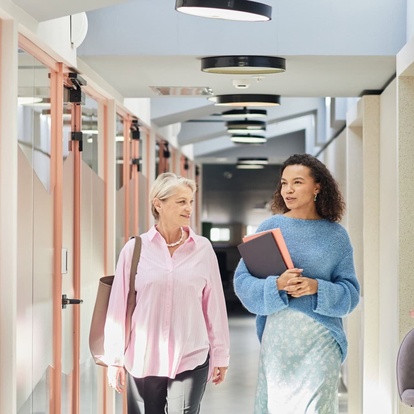 Two woman are walking through an office building talking about the ICF Business Partners