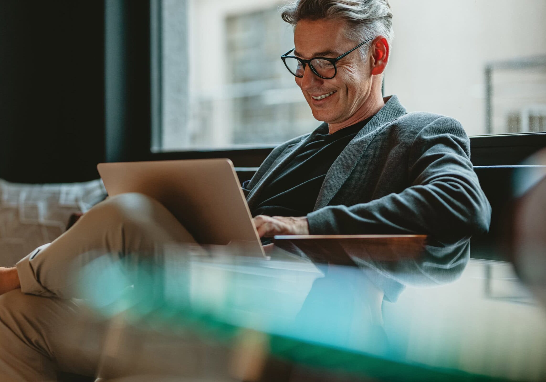 A silver-haired professional coach working comfortably focused credential updates on a laptop in a modern, relaxed office setting.