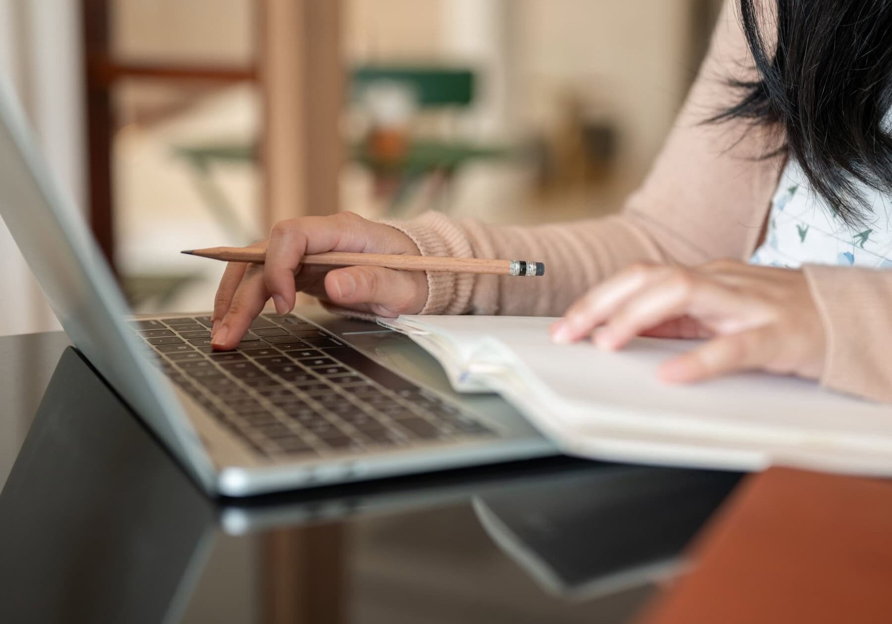 A woman is using a laptop and taking notes form the research portal