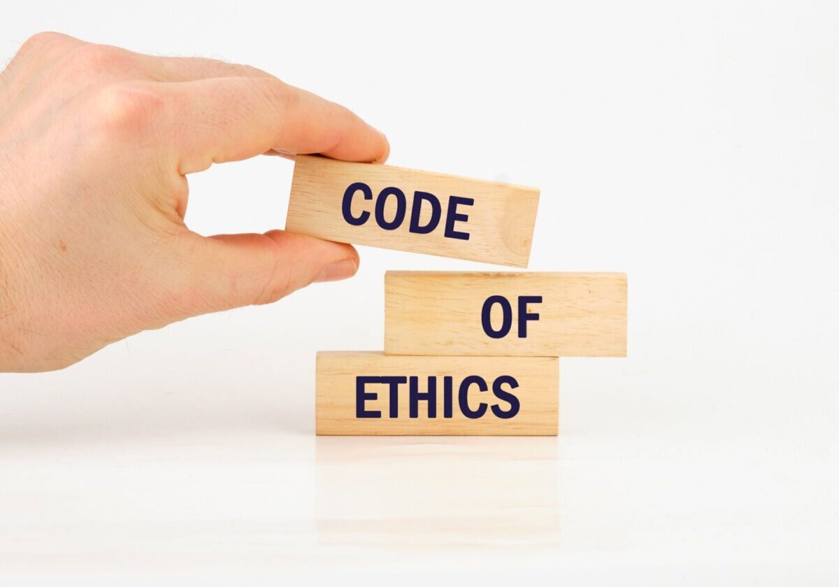 Hand placing a wood block labeled "code” on top of blocks labeled “of” and "ethics.”
