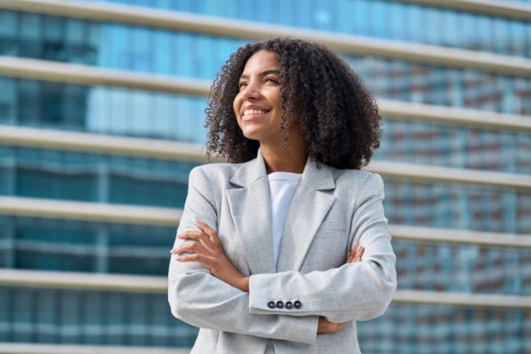 woman smiling with arms crossed in front of large office building