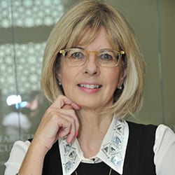 Linda McLoughlin MCC headshot photo, smiling woman with blond hair wearing glasses and business top with her hand at her chin