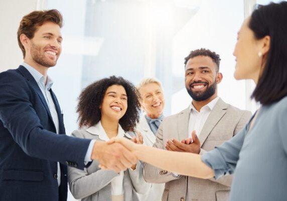 people in a group with one woman shaking a man's hand and everyone looking at the woman