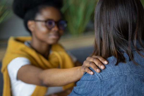 woman with her hand on another woman's shoulder to console her