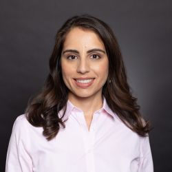 Jessica Signh ACC MD NBC HWC TIPC headshot photo, smiling woman with dark hair wearing light pink top in front of gray background