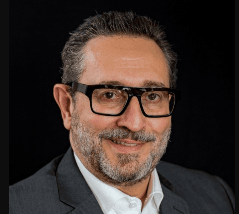 Joano Luiz Pasqual, MCC, headshot, a smiling man is wearing glasses and a button down white shirt with a suit jacket.